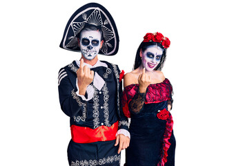 Young couple wearing mexican day of the dead costume over background beckoning come here gesture with hand inviting welcoming happy and smiling