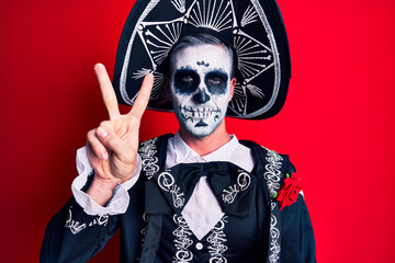 Young man wearing mexican day of the dead costume over red showing and pointing up with fingers...