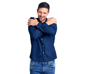 Young handsome man wearing casual shirt hugging oneself happy and positive, smiling confident. self...