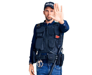 Young handsome man wearing police uniform doing stop sing with palm of the hand. warning expression with negative and serious gesture on the face.