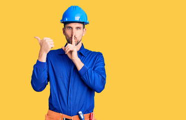 Young handsome man wearing worker uniform and hardhat asking to be quiet with finger on lips pointing with hand to the side. silence and secret concept.