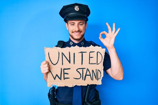 Young caucasian man wearing police uniform holding united we stand banner doing ok sign with fingers, smiling friendly gesturing excellent symbol