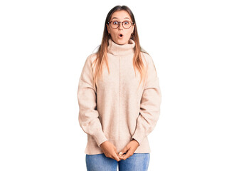 Beautiful caucasian woman wearing wool winter sweater scared and amazed with open mouth for...