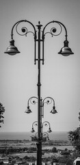 ordered sequence of ancient streetlights through the streets of the city of Tarquinia, Lazio. Vertical photo in black and white. Antique lampposts in a retro atmosphere.