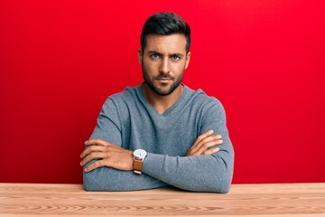 Handsome hispanic man wearing casual style sitting on the table skeptic and nervous, disapproving...