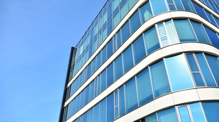 Blue curtain wall made of toned glass and steel constructions under blue sky. A fragment of a...