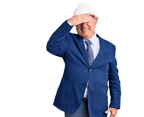 Senior handsome grey-haired man wearing suit and architect hardhat smiling and laughing with hand on face covering eyes for surprise. blind concept.