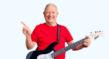 Senior handsome grey-haired man playing electric guitar smiling happy pointing with hand and finger to the side