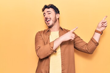 Young hispanic man wearing casual clothes smiling and looking at the camera pointing with two hands and fingers to the side.