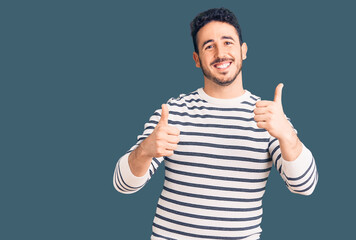 Young hispanic man wearing casual clothes success sign doing positive gesture with hand, thumbs up smiling and happy. cheerful expression and winner gesture.