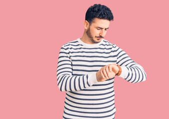 Young hispanic man wearing casual clothes checking the time on wrist watch, relaxed and confident