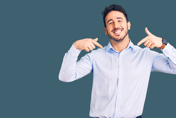 Young hispanic man wearing business clothes looking confident with smile on face, pointing oneself...