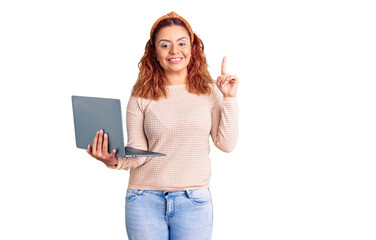 Young latin woman holding laptop surprised with an idea or question pointing finger with happy face, number one