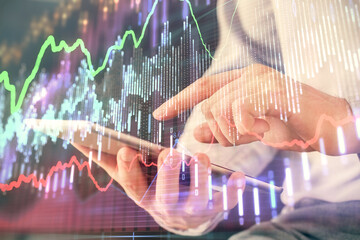 Double exposure of man's hands holding and using a digital device and forex graph drawing. Financial market concept.