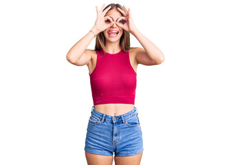 Young beautiful blonde woman wearing elegant summer shirt doing ok gesture like binoculars sticking tongue out, eyes looking through fingers. crazy expression.