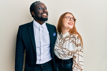 Young interracial couple wearing business and elegant clothes looking away to side with smile on face, natural expression. laughing confident.