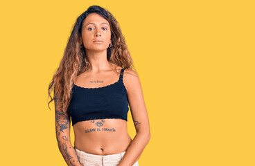 Young hispanic woman with tattoo wearing casual clothes relaxed with serious expression on face. simple and natural looking at the camera.
