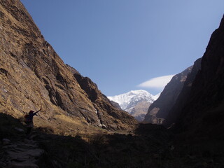 Beautiful Himalayas in the distance with a climber raising her hands in a valley surrounded by shadows, ABC (Annapurna Base Camp) Trek, Annapurna, Nepal