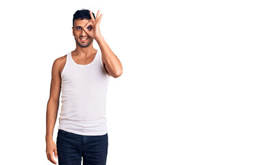 Young hispanic man wearing casual clothes doing ok gesture with hand smiling, eye looking through fingers with happy face.