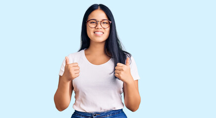 Obraz premium Young beautiful asian girl wearing casual clothes and glasses success sign doing positive gesture with hand, thumbs up smiling and happy. cheerful expression and winner gesture.