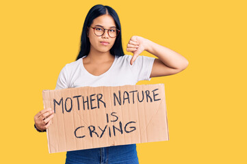 Young beautiful asian girl holding mother nature is crying protest cardboard banner with angry face, negative sign showing dislike with thumbs down, rejection concept