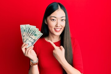 Young chinese woman holding 20 dollars banknote smiling happy pointing with hand and finger