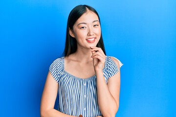 Young chinese woman wearing casual striped t-shirt looking confident at the camera with smile with crossed arms and hand raised on chin. thinking positive.