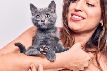 Young beautiful latin woman smilling happy. Standing with smile on face holding adorable cat over isolated white backgroun