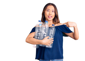 Young beautiful chinese girl holding recycling plastic bottles pointing finger to one self smiling happy and proud