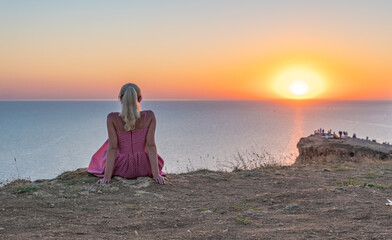 A cheerful girl with a beautiful appearance looks at the sunset with her back in the summer in the evening