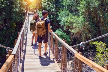 Beautiful couple of hiker wearing explorer clothes and  backpack. Walking on back view at runway over forest landscape background.
