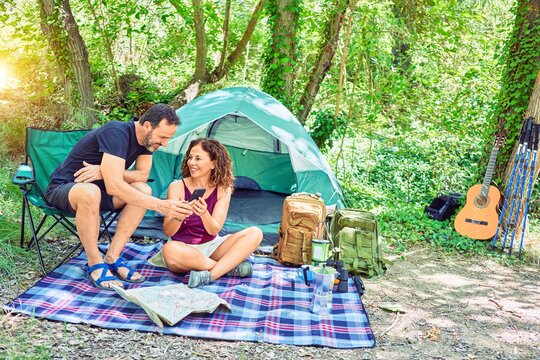 Middle age couple  of hiker smiling happy camping at the forest. Sitting on the floor using smartphone.