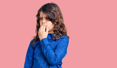 Cute child with long hair wearing casual clothes looking stressed and nervous with hands on mouth biting nails. anxiety problem.