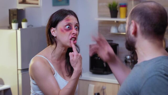 Traumatised woman yelling at drunk man holding a bottle of wine. Abused terrified beaten wife covered in bruises suffering injury from alcoholic violent brutal aggressive husband screeming, fighting.