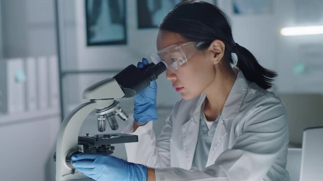 Professional medical researcher sitting table in laboratory working on sample test using microscope and laptop