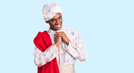 African handsome man wearing tradition sherwani saree clothes laughing nervous and excited with...