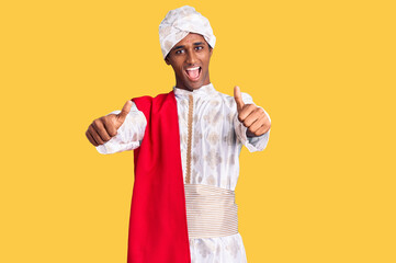 African handsome man wearing tradition sherwani saree clothes approving doing positive gesture with hand, thumbs up smiling and happy for success. winner gesture.