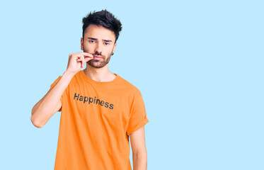 Young hispanic man wearing t shirt with happiness word message mouth and lips shut as zip with...
