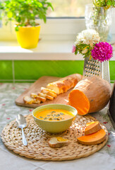 Homemade pumpkin soup in a green pot with pumpkin seeds by the window