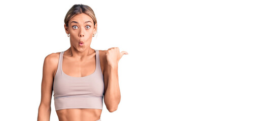 Beautiful caucasian woman wearing sportswear surprised pointing with hand finger to the side, open...