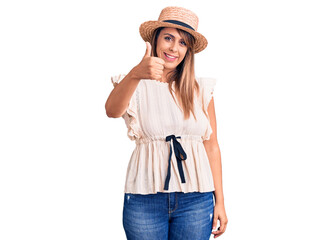 Obraz na płótnie Canvas Young beautiful woman wearing summer hat and t-shirt doing happy thumbs up gesture with hand. approving expression looking at the camera showing success.