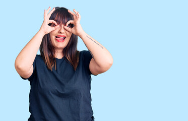 Young plus size woman wearing casual clothes doing ok gesture like binoculars sticking tongue out, eyes looking through fingers. crazy expression.