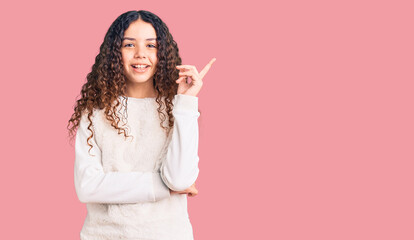 Beautiful kid girl with curly hair wearing casual clothes with a big smile on face, pointing with hand and finger to the side looking at the camera.