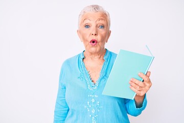 Senior beautiful woman with blue eyes and grey hair reading a book scared and amazed with open mouth for surprise, disbelief face