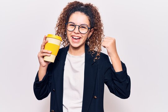 Beautiful kid girl with curly hair wearing business clothes and glasses holding takeaway cup of coffee screaming proud, celebrating victory and success very excited with raised arms