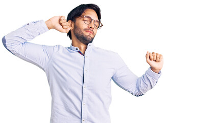 Handsome hispanic man wearing business shirt and glasses stretching back, tired and relaxed, sleepy and yawning for early morning