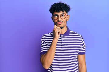 Fototapeta na wymiar Young arab handsome man wearing casual clothes and glasses thinking concentrated about doubt with finger on chin and looking up wondering