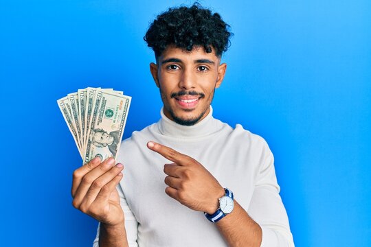 Young arab handsome man holding 20 dollars banknotes smiling happy pointing with hand and finger