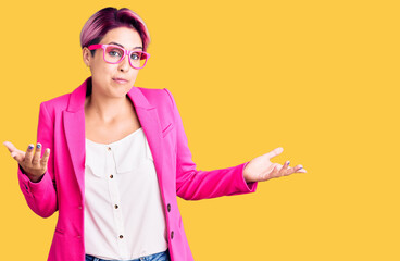 Young beautiful woman with pink hair wearing business jacket and glasses clueless and confused...