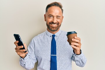 Handsome middle age business man using smartphone and drinking a cup of coffee winking looking at...